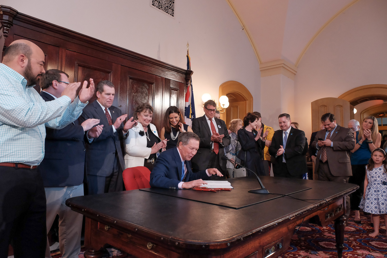 Rep. Seitz looks on as Gov. Kasich signs House Bill 463 which requires most private health insurance policies to include coverage for autism spectrum disorders on April 12, 2017.