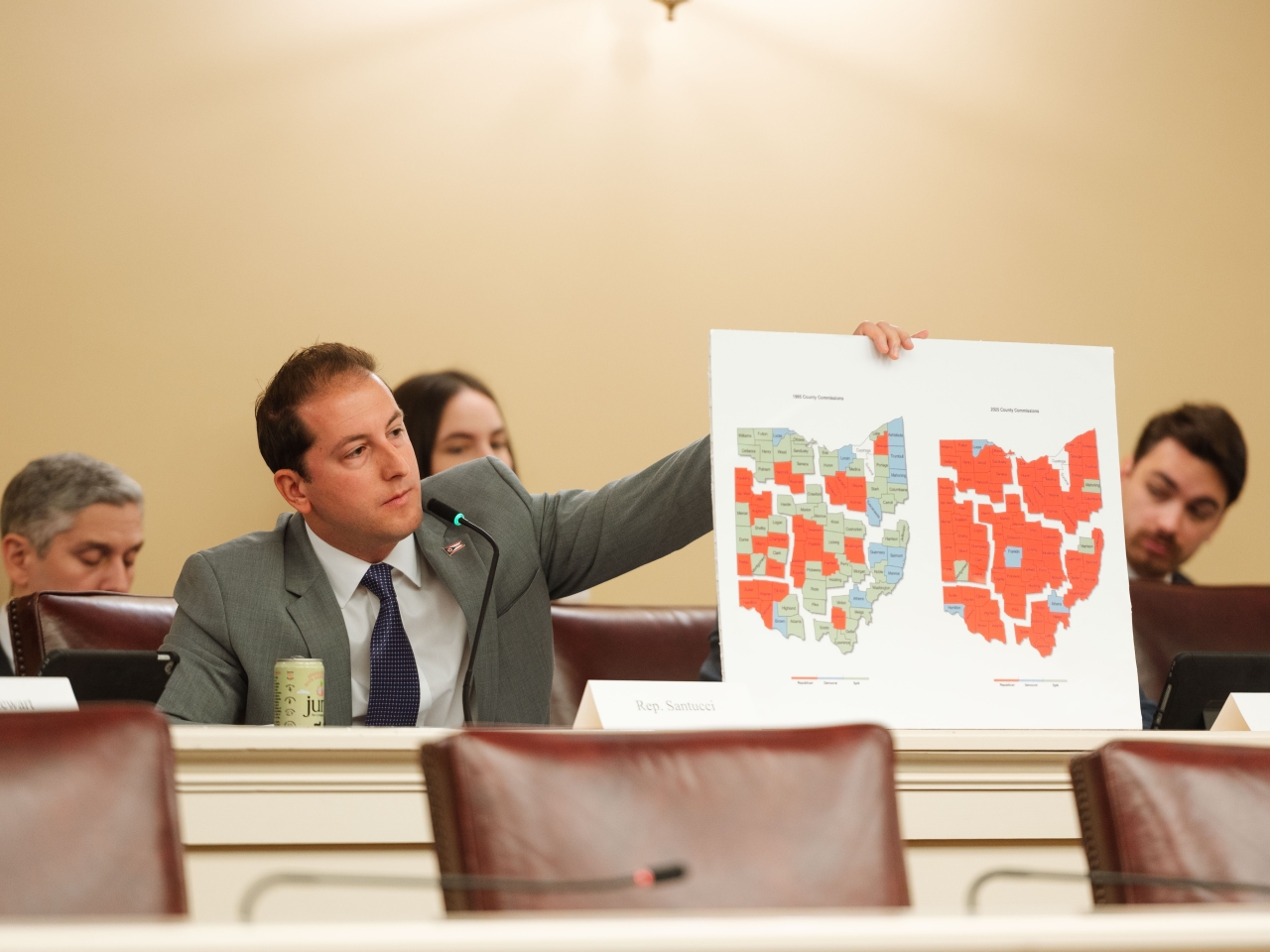 Rep. Santucci holds up two county commissioner maps during the Joint Committee on Congressional Redistricting