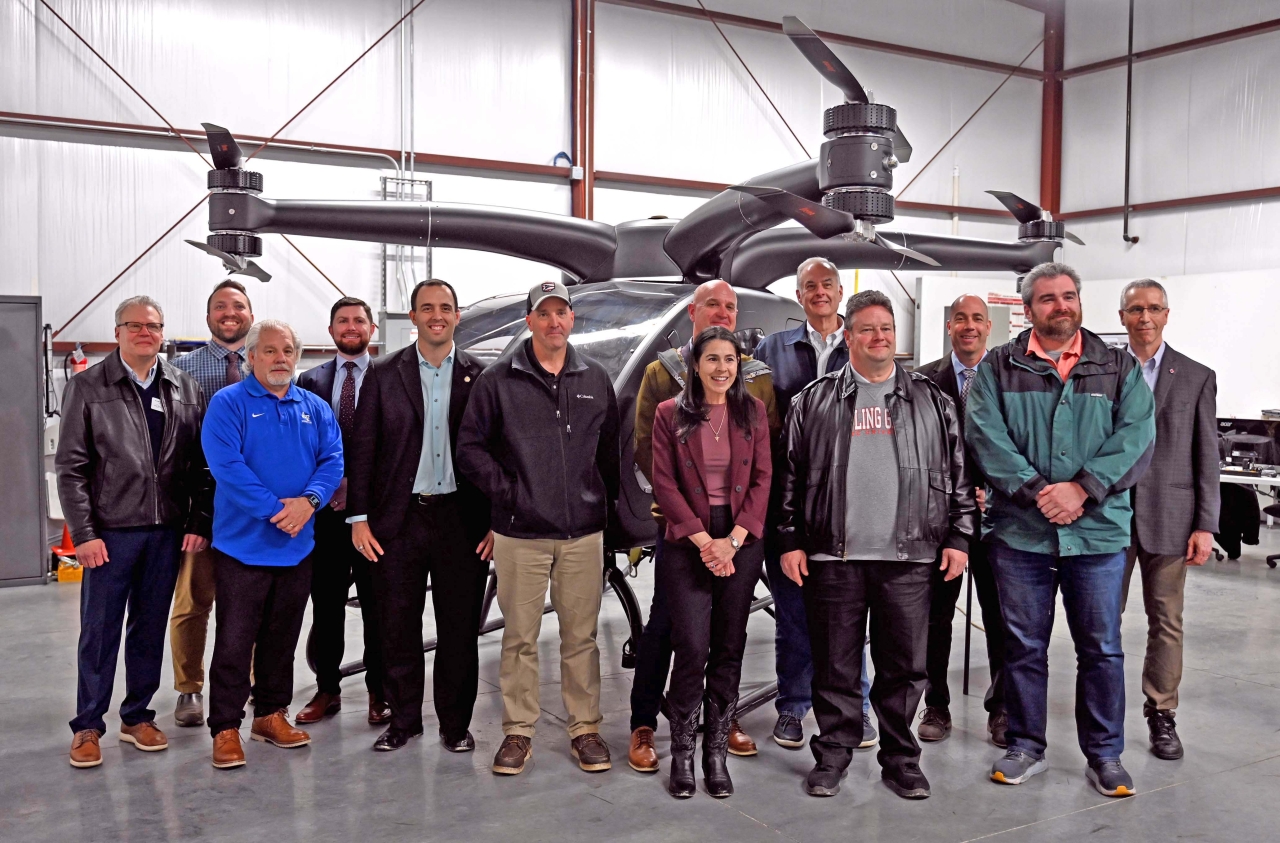 State Representative Bernie Willis posses with members of the House Aviation and Aerospace Committee in front of an EVTOL drone at Springfield Berkley Municipal Airport.