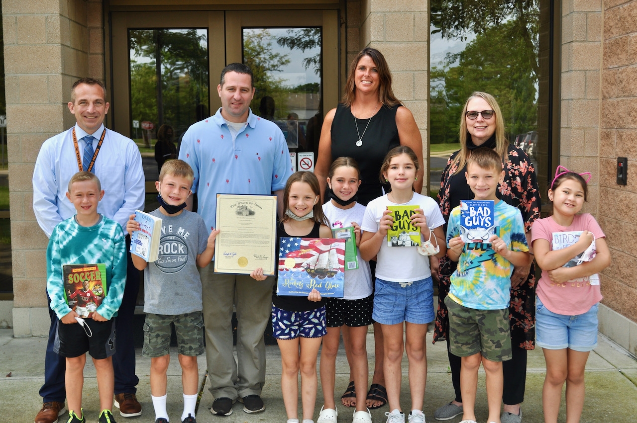 Photo: Representative Kris Jordan (R-Ostrander), center, is joined by Schultz Elementary School students (left to right) Max Woodruff, Alexander Emmons, Aurora Larson, Adalynn Singleton, Kaitlyn Brooks, Conner Bower and Bailey Chappell, as well as Principal Travis Woodworth (left), Superintendent Heidi Kegley (center) and LMC Assistant Rose Long (right).
